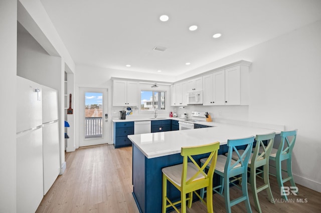 kitchen with white cabinetry, a breakfast bar area, kitchen peninsula, white appliances, and light hardwood / wood-style flooring