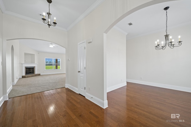 interior space with ceiling fan with notable chandelier, a tiled fireplace, ornamental molding, and dark wood-type flooring