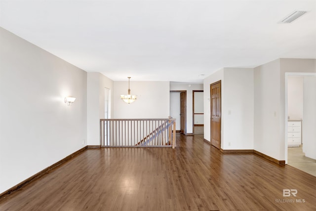 unfurnished room featuring baseboards, a notable chandelier, visible vents, and wood finished floors