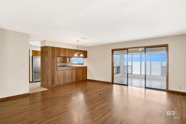 unfurnished living room featuring baseboards, a water view, and wood finished floors