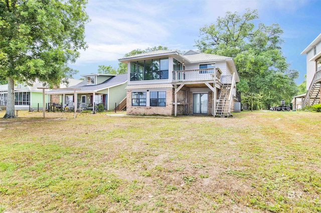 view of front of home with a front yard, a wooden deck, a sunroom, brick siding, and stairs