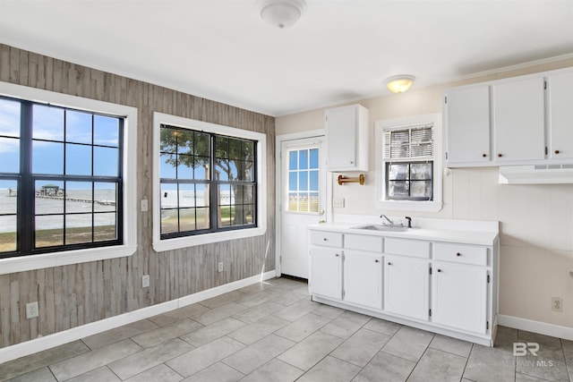 kitchen with baseboards, a sink, white cabinets, and wood walls