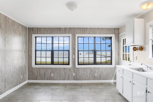 interior space with wood walls, a sink, baseboards, white cabinets, and light countertops