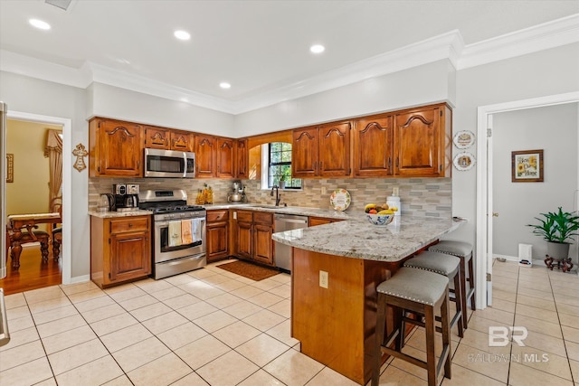 kitchen featuring appliances with stainless steel finishes, crown molding, light tile patterned floors, and a breakfast bar