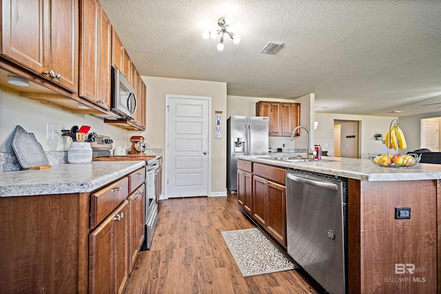 24189 Harvester Dr, Loxley, AL 36551 - kitchen featuring stainless steel appliances, wood finished floors, brown cabinetry, light countertops, and a center island with sink
