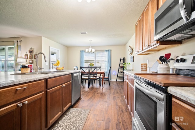 24189 Harvester Dr, Loxley, AL 36551 - kitchen featuring stainless steel appliances, brown cabinetry, a chandelier, dark wood finished floors, and hanging light fixtures