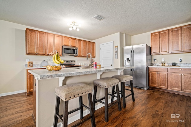 24189 Harvester Dr, Loxley, AL 36551 - kitchen featuring appliances with stainless steel finishes, dark wood finished floors, light countertops, brown cabinetry, and a breakfast bar area