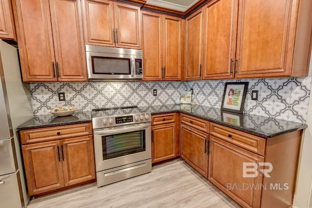 20752 Southwood St, Fairhope, AL 36532 - kitchen featuring stainless steel appliances, dark stone countertops, brown cabinetry, light wood-style flooring, and decorative backsplash