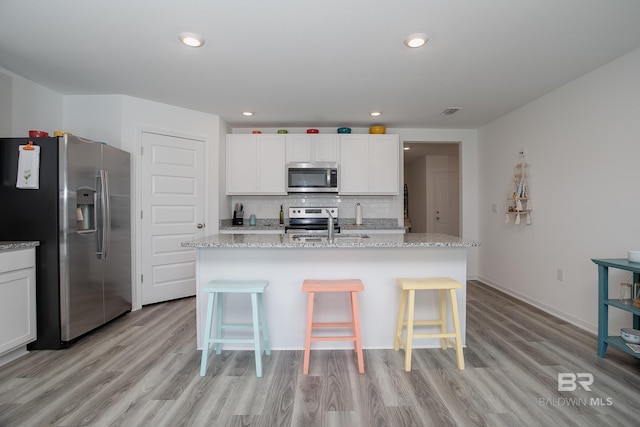 kitchen featuring light stone countertops, a center island with sink, appliances with stainless steel finishes, and white cabinets