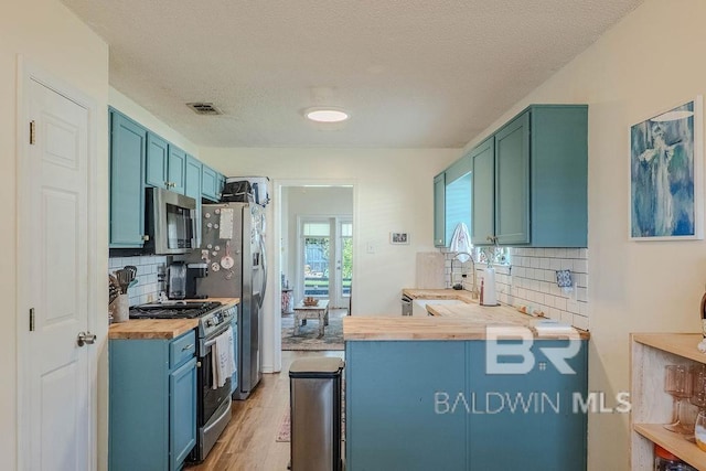 kitchen with a textured ceiling, backsplash, stainless steel appliances, light hardwood / wood-style floors, and butcher block counters