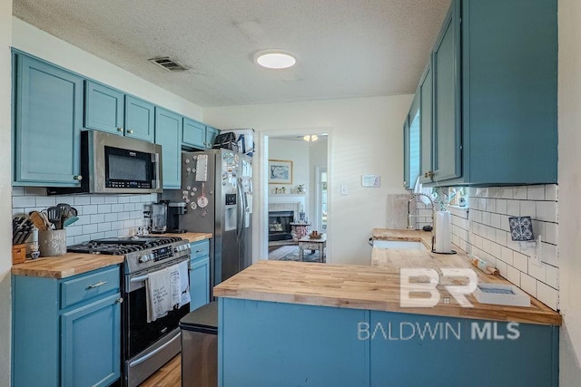 kitchen featuring blue cabinets, stainless steel appliances, backsplash, and wooden counters