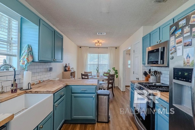 kitchen with butcher block countertops, decorative backsplash, sink, and stainless steel appliances