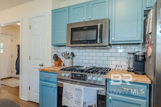 kitchen featuring blue cabinets, tasteful backsplash, wooden counters, hardwood / wood-style flooring, and appliances with stainless steel finishes