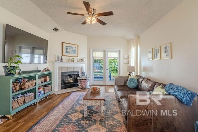 living room featuring wood-type flooring, a tiled fireplace, vaulted ceiling, and a textured ceiling