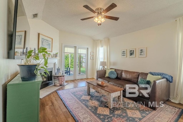 living room featuring ceiling fan, light wood-type flooring, lofted ceiling, and a textured ceiling