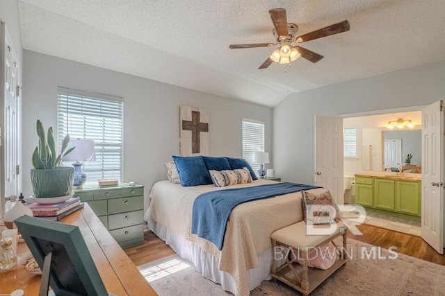 bedroom with ceiling fan, lofted ceiling, connected bathroom, a textured ceiling, and light hardwood / wood-style floors