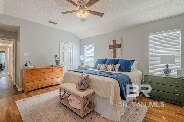 bedroom with hardwood / wood-style flooring, ceiling fan, vaulted ceiling, and a textured ceiling