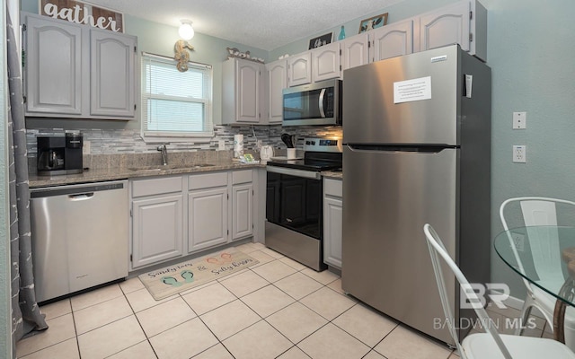 kitchen with backsplash, sink, light tile patterned flooring, appliances with stainless steel finishes, and a textured ceiling