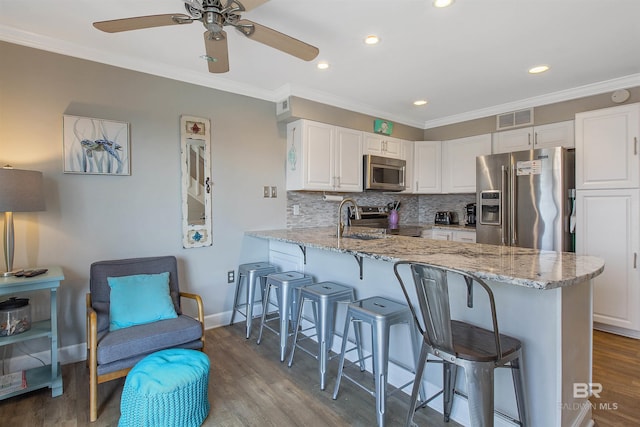 kitchen with light stone counters, appliances with stainless steel finishes, a kitchen bar, and visible vents