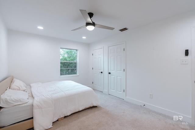 bedroom featuring ceiling fan, light carpet, and two closets