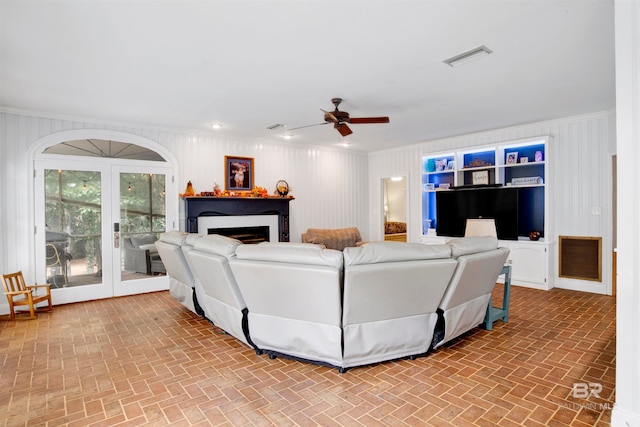 living room featuring french doors, ceiling fan, crown molding, and wood walls