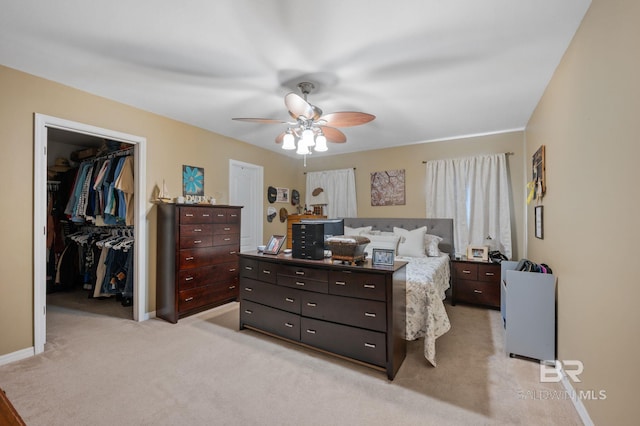 bedroom with baseboards, ceiling fan, a closet, light carpet, and a walk in closet