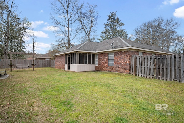 back of house with brick siding, a lawn, a fenced backyard, and a sunroom