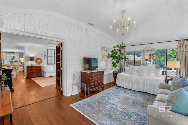 bedroom featuring dark hardwood / wood-style floors, brick wall, vaulted ceiling, and a notable chandelier