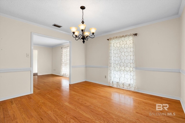 spare room featuring plenty of natural light, light hardwood / wood-style floors, ornamental molding, and an inviting chandelier