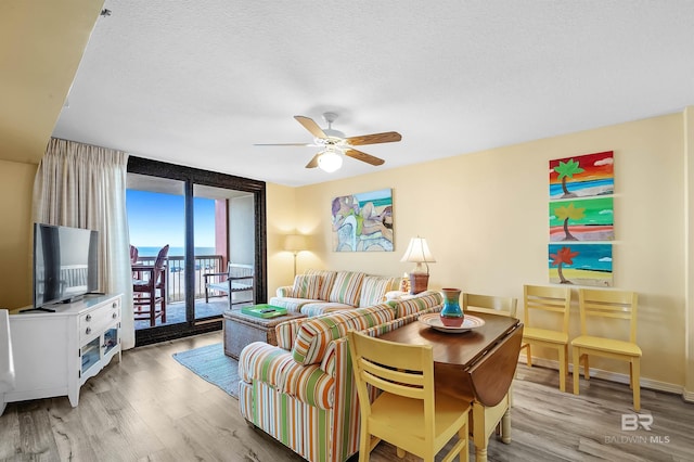 living room featuring ceiling fan, light hardwood / wood-style flooring, floor to ceiling windows, and a textured ceiling