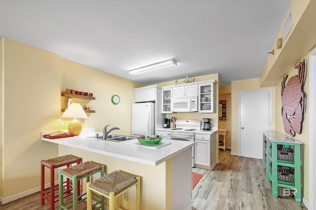 kitchen featuring sink, a kitchen breakfast bar, kitchen peninsula, white appliances, and white cabinets