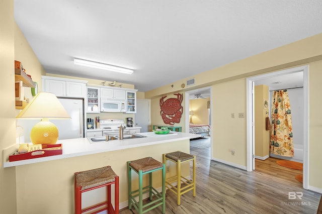 kitchen with sink, a breakfast bar area, white cabinets, kitchen peninsula, and white appliances