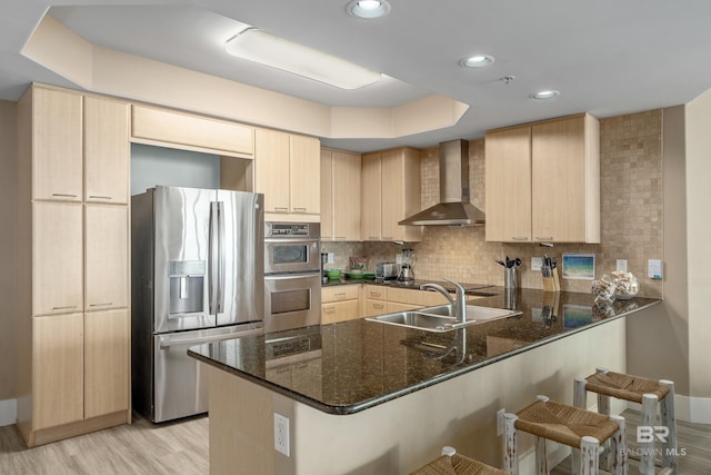 kitchen with wall chimney range hood, kitchen peninsula, dark stone countertops, sink, and stainless steel appliances