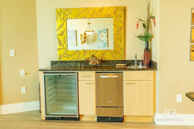 bar with wine cooler, light brown cabinets, light wood-type flooring, and dark stone countertops