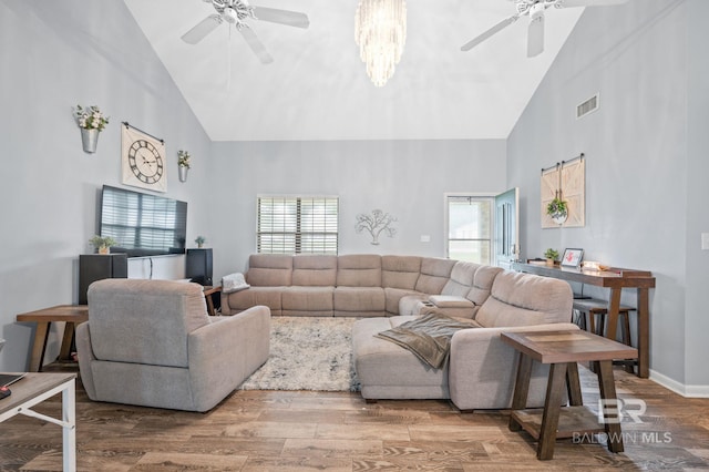 living room with ceiling fan with notable chandelier, high vaulted ceiling, and hardwood / wood-style flooring