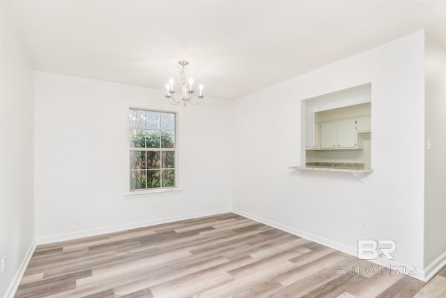 spare room featuring light wood-style floors, baseboards, and an inviting chandelier