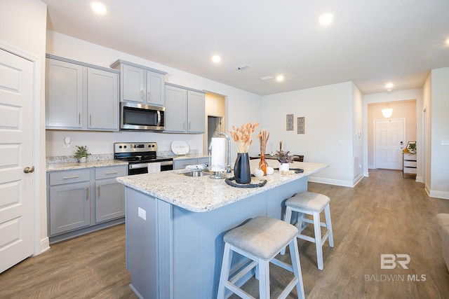 kitchen with sink, a center island with sink, appliances with stainless steel finishes, a breakfast bar, and light hardwood / wood-style floors