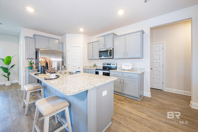 kitchen featuring sink, a kitchen island with sink, light hardwood / wood-style flooring, stainless steel appliances, and a kitchen bar