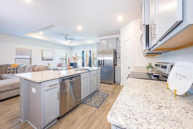 kitchen with light hardwood / wood-style floors, a kitchen island with sink, sink, appliances with stainless steel finishes, and light stone countertops