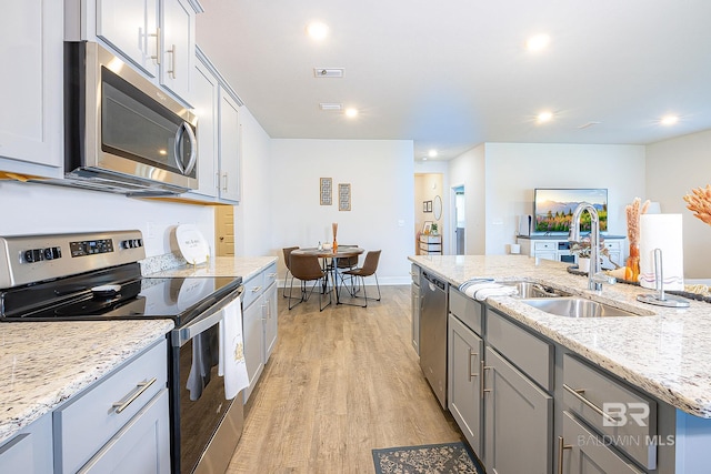 kitchen with sink, a kitchen island with sink, light hardwood / wood-style flooring, appliances with stainless steel finishes, and light stone countertops