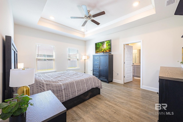 bedroom with light wood-type flooring, a tray ceiling, connected bathroom, and ceiling fan