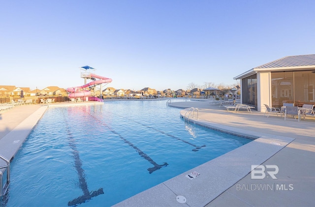 view of pool with a sunroom, a water slide, and a patio area