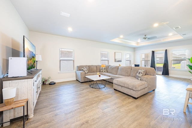 living room featuring light hardwood / wood-style flooring, ceiling fan, and a raised ceiling