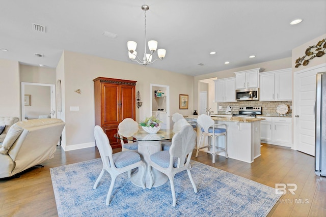 dining room with washer / clothes dryer, visible vents, a notable chandelier, and wood finished floors