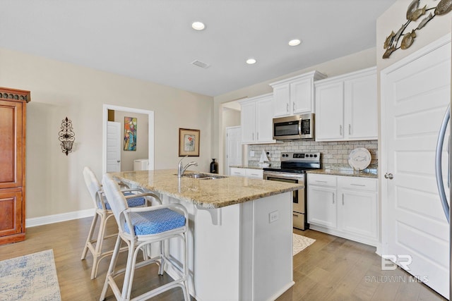 kitchen featuring light stone counters, stainless steel appliances, backsplash, a sink, and an island with sink