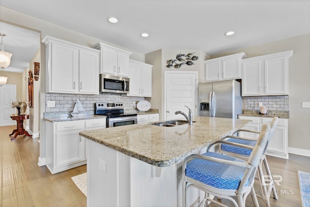 kitchen with light wood finished floors, appliances with stainless steel finishes, white cabinets, and a sink