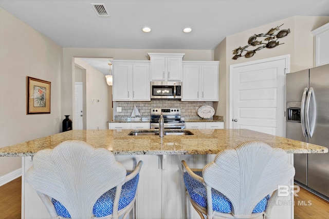 kitchen featuring stainless steel appliances, visible vents, backsplash, white cabinets, and a sink