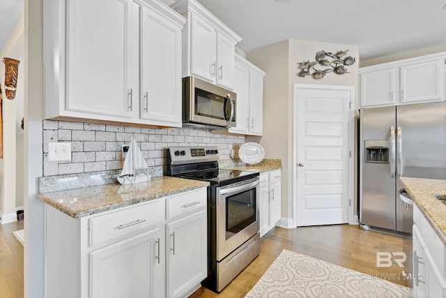 kitchen featuring light stone counters, light wood-style flooring, stainless steel appliances, white cabinets, and tasteful backsplash