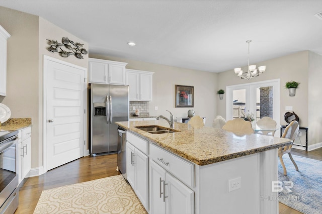 kitchen with light stone counters, stainless steel appliances, backsplash, white cabinetry, and a sink