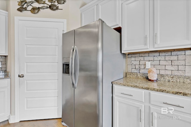 kitchen featuring light wood-style floors, white cabinets, stainless steel refrigerator with ice dispenser, light stone countertops, and tasteful backsplash